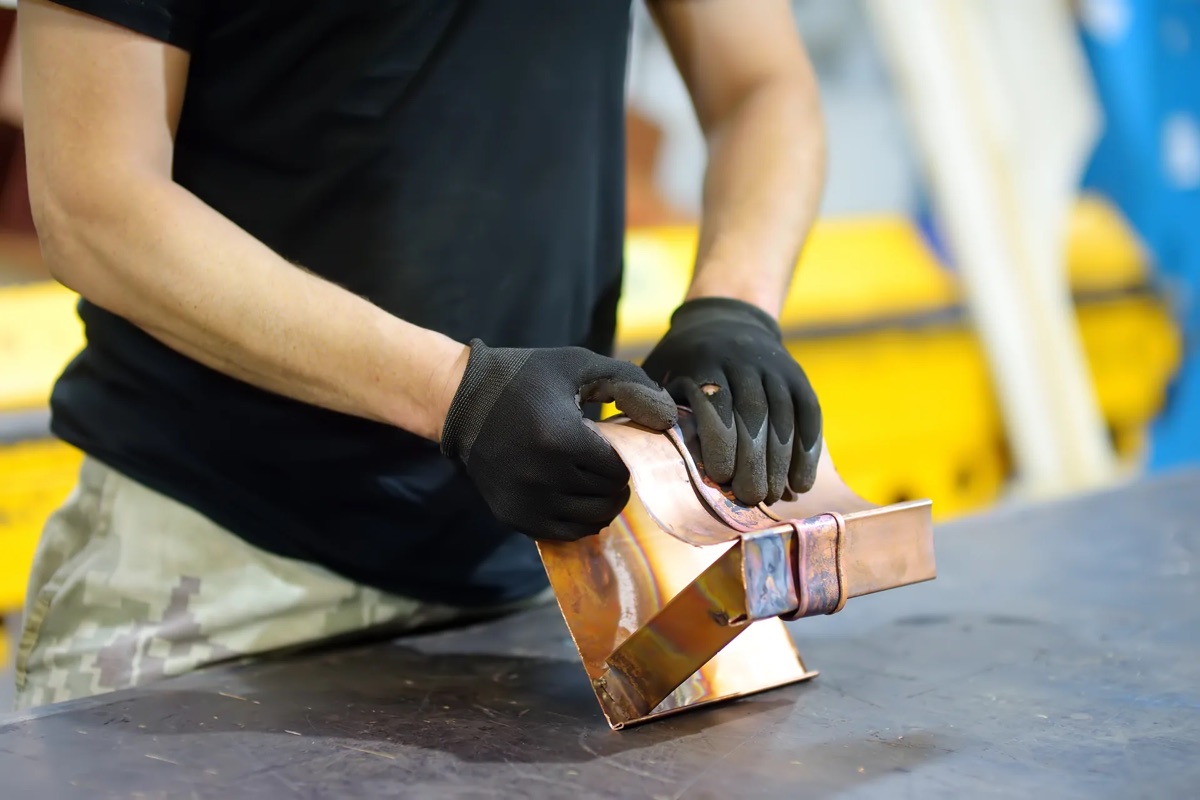 Gloved craftsman assembling a soldered copper piece at the workbench